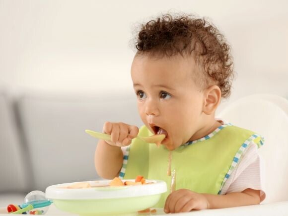 baby eating with bib on with a spoon and bowl