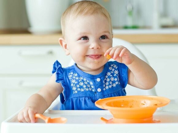 9 month old girl eating with spoon and bowl
