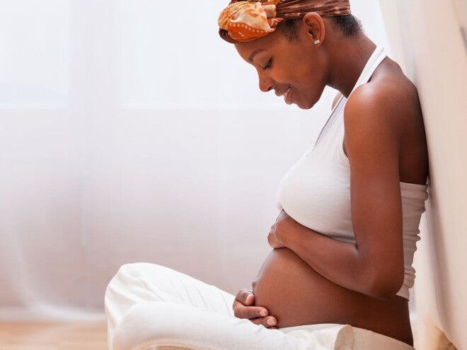 Pregnant woman in white pants and top holding her belly