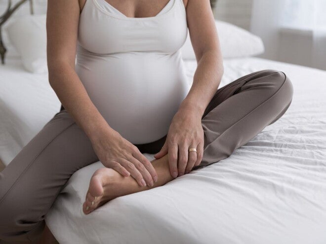 Pregnant woman in white shirt and grey pants sitting on a bed