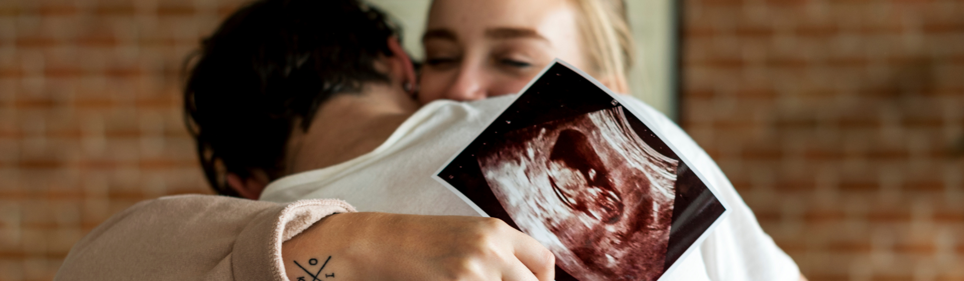 Woman hugging partner with ultrasound image in her hand